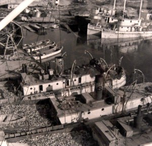 Aerial view of menhaden boats, looking loaded with fish to the scuppers, at one of the Beaufort fish factories, date unknown. You can see a net reel (for drying purse seines) on the upper left, and a trio of purse boats beneath the reel.