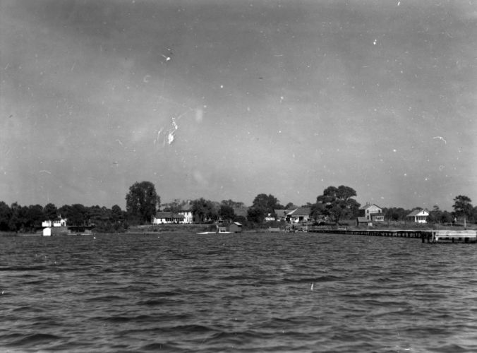 The village of Marines, ca. 1938-41, as seen from a boat on the New River. You can see Ollie Marine's general store immediately at the foot of the community wharf, partly obscured by a large oak. If you look close, you can also see the roof of his blacksmithing shed just to the left of the store. His gristmill is located on the far side of the store, so is not visible seen in this photograph. The store was located a dirt road that ended at the wharf.