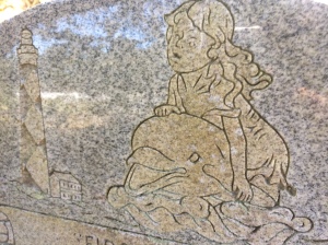 A detail from the grave marker for Celia Faye Styron. Above her name, the marker reads, "First Mate." Next to her marker, a marker for Louis C. Styron, Jr. reads, "Skipper" and features a carving of the Cape Lookout Lighthouse and a sailing vessel.