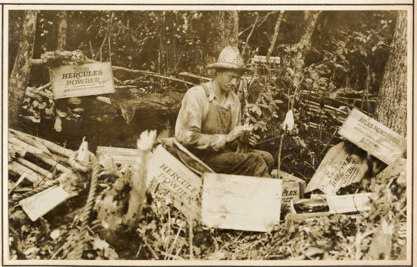 One of derrick barge<em> No. 14's</em> crewmen preparing a dynamite for blasting root stumps on the banks of the Scuppernong River, May 1931. Judging by the box labels, he was using dynamite produced by the Hercules Powder Co. and the Atlas Powder Company, two of the chemical and munitions companies that were formed after the federal courts broke up Du Pont's munitions monopoly in 1911-12.  Source: Office of History, HQ, U.S. Army Corps of Engineers
