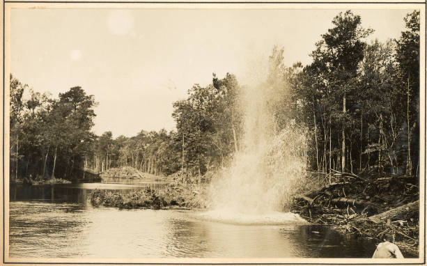 Here we can see one of the dynamite blasts that the <em>No. 14's</em> crew used to uproot stumps, roots, and earth and straighten the Scuppernong River near Creswell, N.C., May 1931. After uprooting the largest stumps and breaking up the earth with dynamite, the crewmen would get to work with the dredge barge's bucket. Source: Office of History, HQ, U.S. Army Corps of Engineers