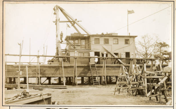 A workman standing high above derrick barge No. 14's deck, apparently working on the A-frame, February 1932. At the time, the barge was in dry dock for repairs and maintenance at a boatyard in Elizabeth City, N.C. She had had a busy year in 1931. In addition to her duty on the Scuppernong River, Knobbs Creek, and Turners Cut, she had also undertaken at least 2 other large projects: clearing snags and other obstructions along a 35-mile-long stretch of the Roanoke River and removing shoals and clearing obstructions from the mouth of the Meherrin River to Murfreesboro, a distance of 12 miles. In September 1931, she had also had a brief stint clearing mud, roots, and logs out of the Dismal Swamp Canal's lock in South Mills, N.C. Source: Office of History, HQ, U. S. Army Corps of Engineers