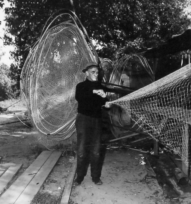 A bow net maker at work on the Roanoke River, ca. 1940. Crafted of ash wood, the nets had long handles and could be wielded by a single individual. Fishermen and women alike treasured their bow nets. They were often objects of great pride, and many fishermen and women passed their bow nets down to their children and grandchildren. Back in 2006, the year before the herring ban was enacted, my story <a href="https://www.ncpedia.org/listening-to-history/jones-alice">"Alice Eley Jones: Herring Fish"</a> recalled a herring fisherman's affection for the handmade bow net he used on the Meherrin River." Photo courtesy, State Archives of North Carolina